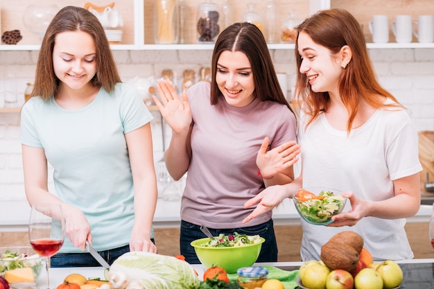 Healthy eating. Balanced diet. Happy young females cooking green salad. Organic foods assortment around.