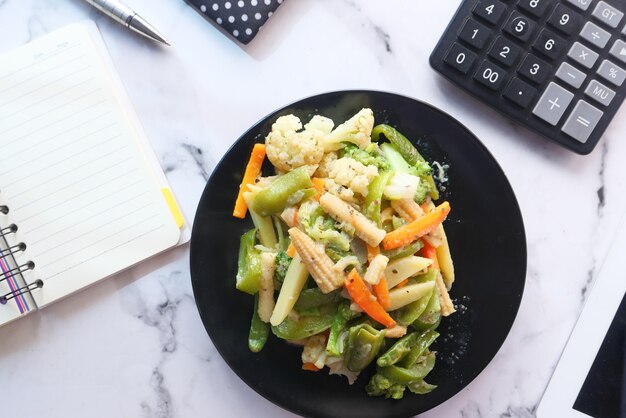 Healthy eating concept of fresh cooked vegetables on plate on office table .