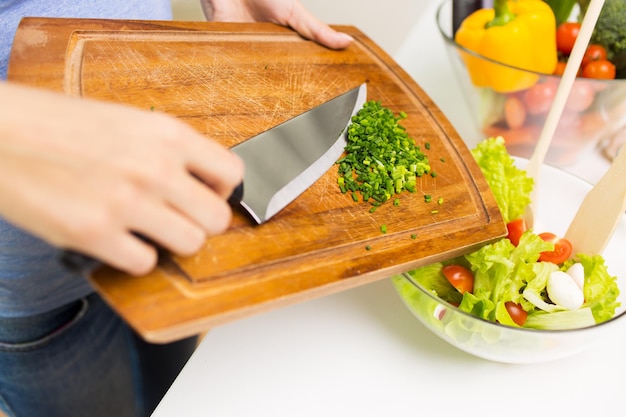 healthy eating, cooking, vegetarian food, diet and people concept - close up of woman adding chopped green onion to salad