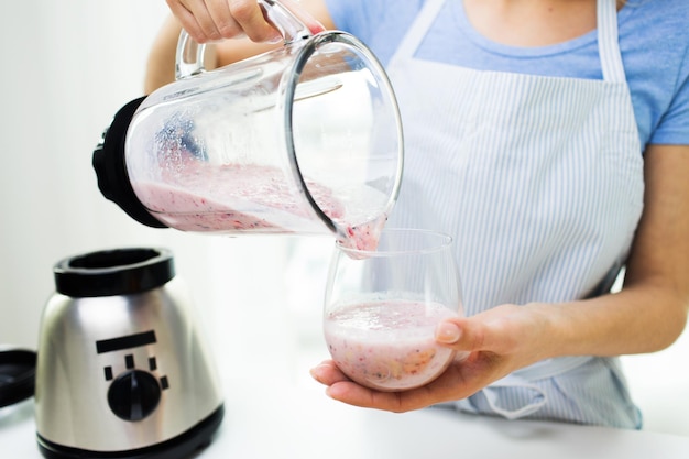 healthy eating, cooking, vegetarian food, dieting and people concept - close up of young woman pouring fruit shake from blender shaker jug to glass at home