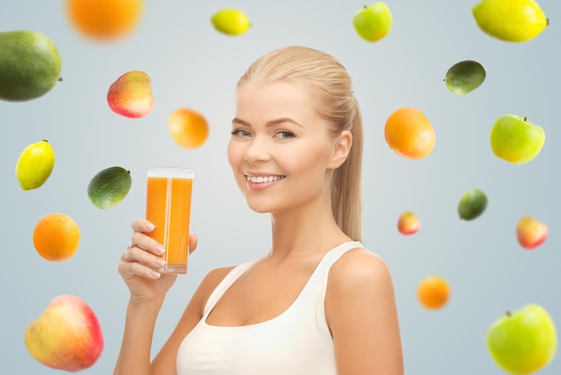 healthy eating, diet, detox and people concept - happy young woman holding glass of orange juice over gray background with falling fruits