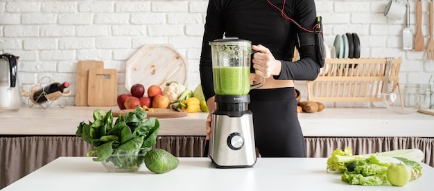 Healthy eating, dieting concept. Young blond smiling woman making green smoothie at home kitchen