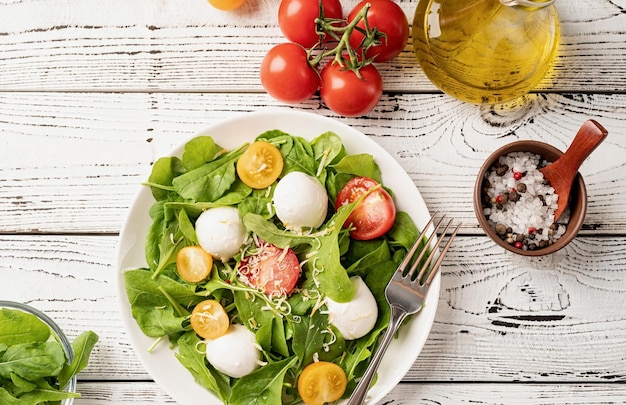 Alimentazione sana e dieta insalata fresca con rucola, pomodorini, mozzarella e formaggio a pasta dura su fondo di legno bianco vista dall'alto