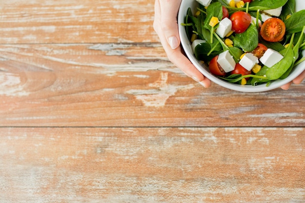 healthy eating, dieting and people concept - close up of young woman hands with salad bowl on blank table at home