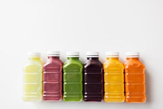 Фото Здоровое питание, напитки, диета и концепция детоксикации - крупный план пластиковых бутылок с различными фруктовыми или овощными соками на белом