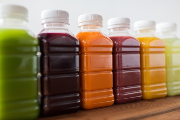концепция здорового питания, напитков, диеты и упаковки - крупный план пластиковых бутылок с различными фруктовыми или овощными соками на деревянном столе