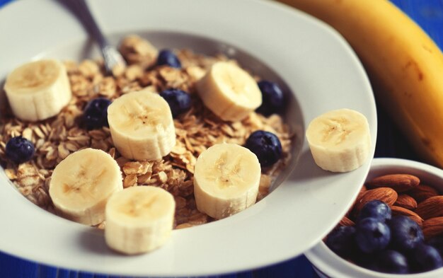 Cibo sano e concetto di dieta farina d'avena con frutti di bosco noci e banane piatto bianco blu sullo sfondo di legno