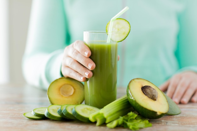 healthy eating, food, dieting and people concept - close up of woman hands with green fresh juice and vegetables sitting at table