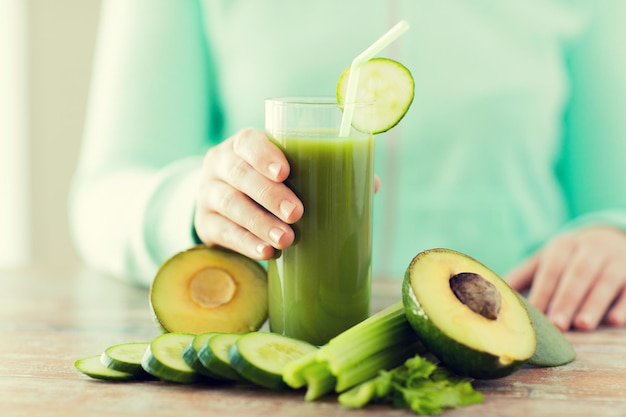 healthy eating, food, dieting and people concept - close up of woman hands with green fresh juice and vegetables sitting at table