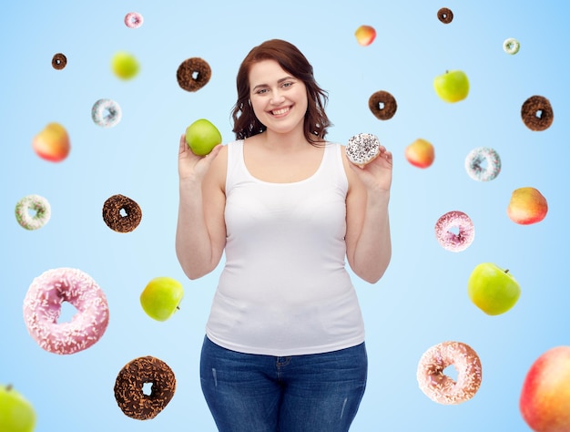건강한 식습관, 정크 푸드, 다이어트 및 선택적인 사람들의 개념 - 파란 배경 위에 사과와 도넛 사이에서 선택하는 미소와 크기의 여성