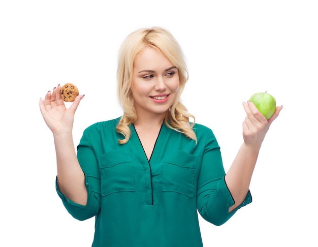 healthy eating, junk food, diet and choice people concept - smiling woman choosing between apple and cookie