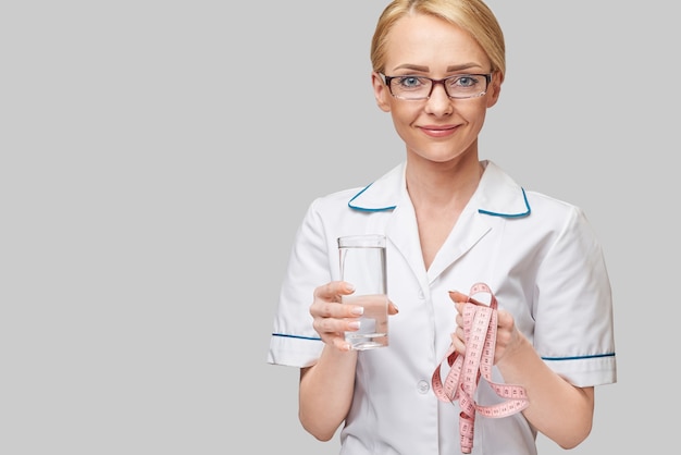 Healthy eating or lifestyle concept - female woman doctor holding and a glass of clear fresh water and measure tape