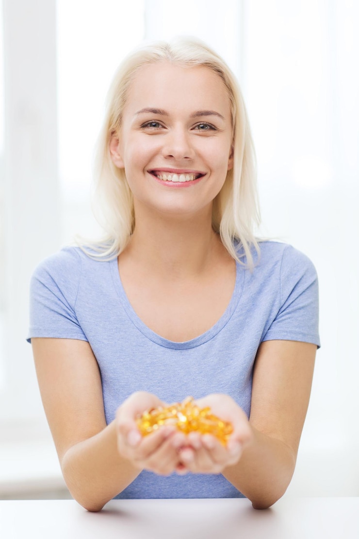 Photo healthy eating, medicine, health care, food supplements and people concept - happy woman holding handful of fish oil capsules at home