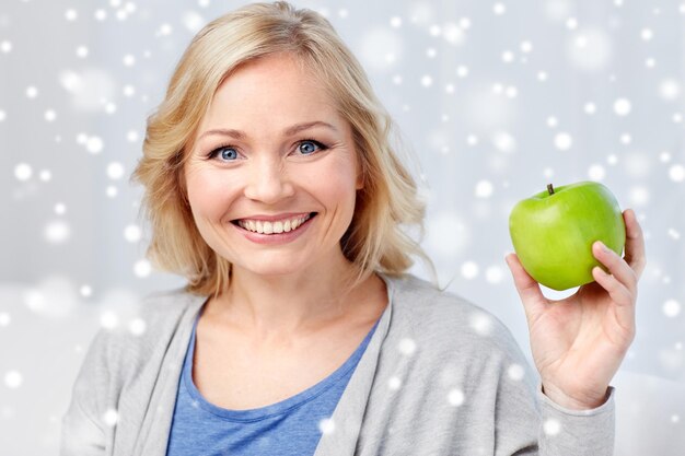 Foto alimentazione sana, cibo biologico, frutta, dieta e concetto di persone - donna di mezza età felice con mela verde a casa sopra la neve