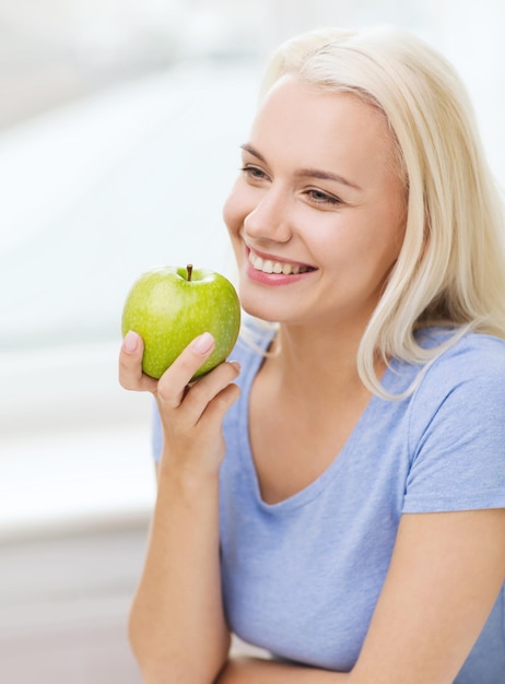 healthy eating, organic food, fruits, diet and people concept - happy woman eating green apple at home