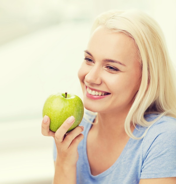 건강한 식생활, 유기농 식품, 과일, 다이어트, 그리고 사람들의 개념 - 집에서 녹색 사과를 먹는 행복한 여성