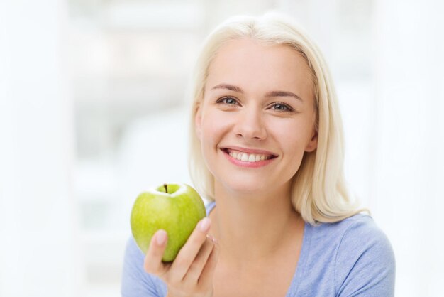 健康的な食事、有機食品、果物、食事、人々 のコンセプト - 家で青リンゴを食べて幸せな女