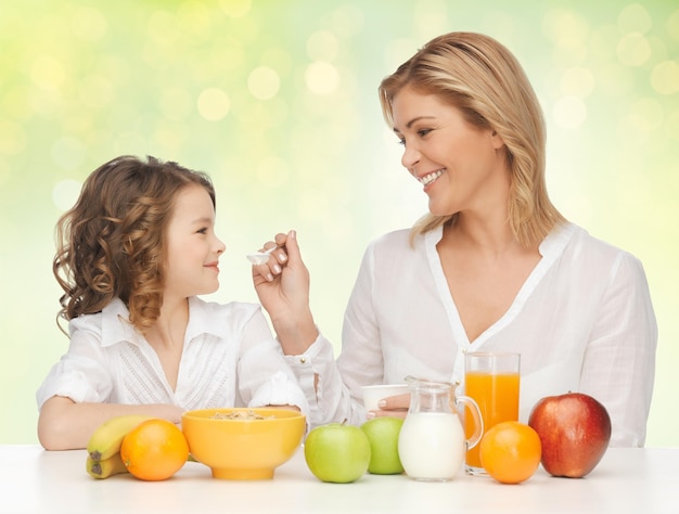 healthy eating, people, family and food concept - happy mother and daughter having breakfast over green holidays lights background