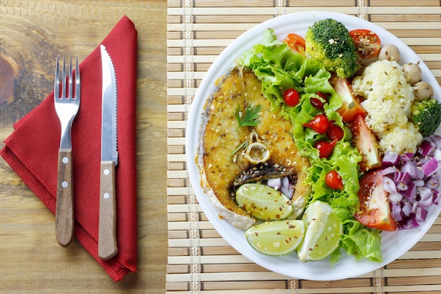 素朴な木製のテーブルの上にグリルした魚と野菜のサラダの健康的な食事プレートケトジェニックと旧石器時代の食事