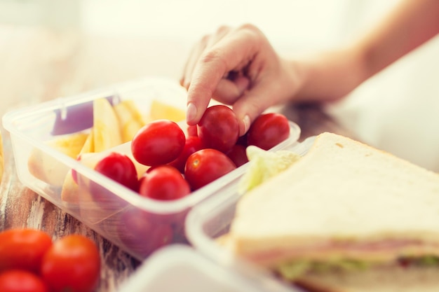 healthy eating, storage, dieting and people concept - close up of woman with food in plastic container at home kitchen