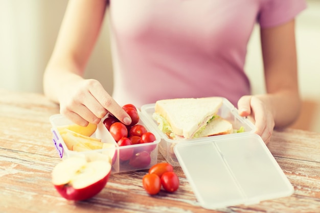 healthy eating, storage, dieting and people concept - close up of woman with food in plastic container at home kitchen