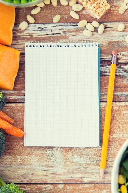 Healthy eating, vegetarian food, advertisement and culinary concept - close up of ripe vegetables and notebook with pencil on wooden table