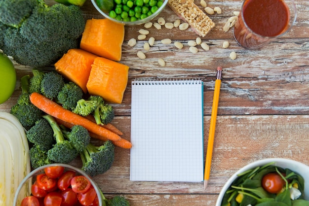 Healthy eating, vegetarian food, advertisement and culinary concept - close up of ripe vegetables and notebook with pencil on wooden table