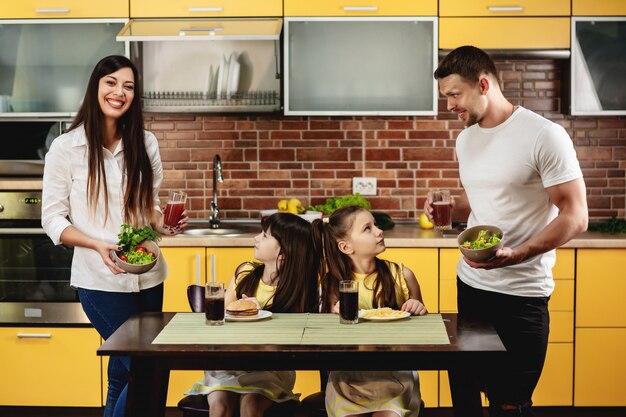 Alimentazione sana vs cattive abitudini. i genitori offrono alle loro figlie un'insalata con succo invece di un hamburger e una bibita. le bambine non sono felici. concetto di cibo spazzatura