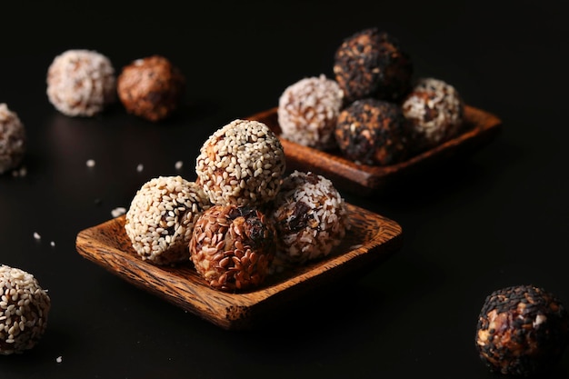 Healthy energy balls of nuts oatmeals and dried fruit with coconut flax and sesame seeds on wooden coconut plates on a black background horizontal orientation