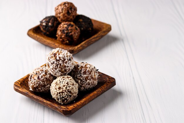 Healthy energy balls of nuts, oatmeals and dried fruit with coconut, flax and sesame seeds on wooden coconut plates on a white background, horizontal orientation, copy space