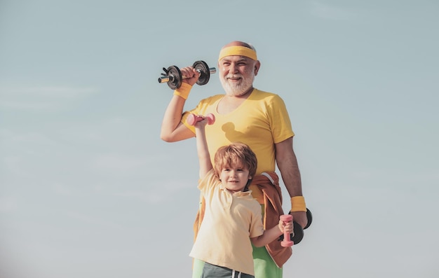 Healthy family lifestyle grandfather and little grandson practice dumbbells exercises outdoors motiv