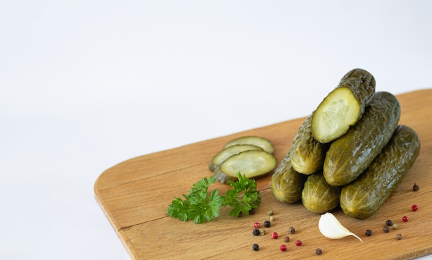 Healthy fermented sliced gherkins or cucumbers with herbs and spices on rustic wooden board isolated on white