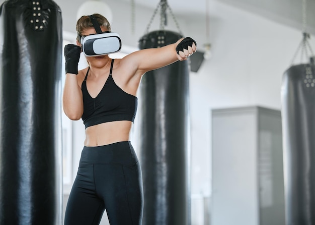 VR 헤드셋을 착용한 건강하고 활동적인 권투 여성이 훈련을 하고 체육관에서 운동하는 동안 메타버스에 액세스합니다. 기술을 사용하여 가상 현실에서 운동하는 여성 권투 선수