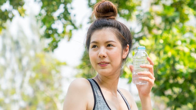 健康的なフィット感としっかりとしたスリムな十代の女の子は、手にプラスチックボトルから水を飲む