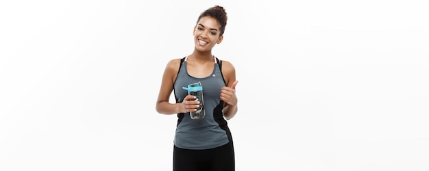 Healthy and Fitness concept beautiful African American girl in sport clothes holding water bottle after workout Isolated on white studio background