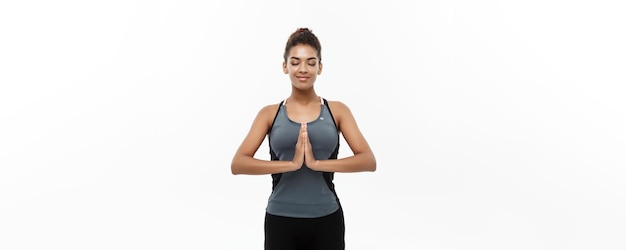 Concetto di salute e fitness bella signora africana americana in abbigliamento fitness facendo yoga e meditazione isolata su sfondo bianco