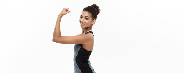 Healthy and Fitness concept Portrait of young beautiful African American showing her strong muscle with confident cheerful facial expression Isolated on white studio background