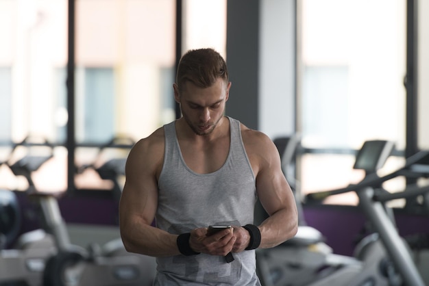 Healthy Fitness Man Using Smartphone While Resting In The Gym