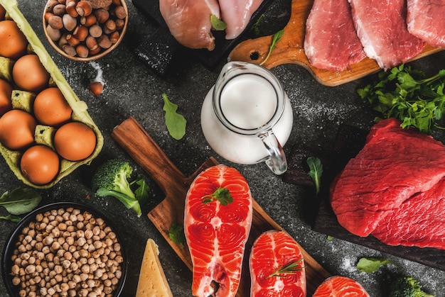 Healthy food background. Selection of protein sources: beef and pork meat, chicken  filet, salmon fish, egg, beans, nuts, milk. Top view copyspace, dark background