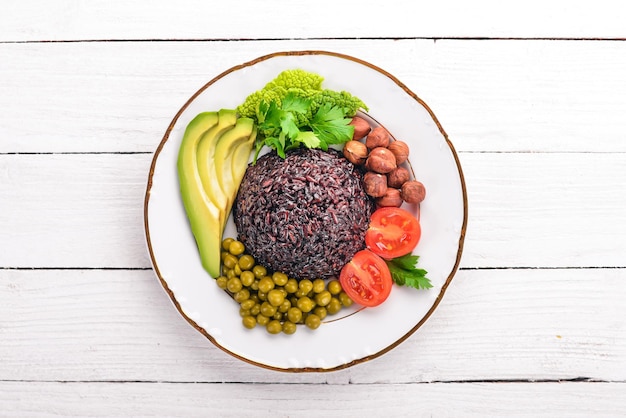 Healthy food Black rice avocado cherry tomatoes green peas and hazelnut On a wooden background Top view Free space for your text