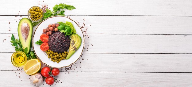 Healthy food black rice avocado cherry tomatoes green peas and\
hazelnut on a wooden background top view free space for your\
text