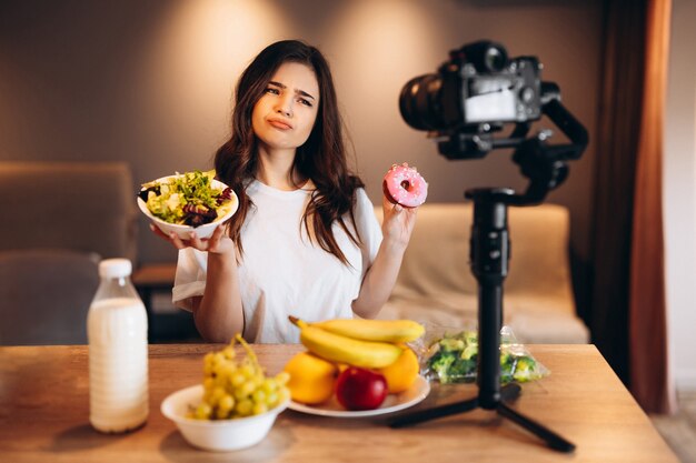 Healthy food blogger young female cooking fresh vegan salad of fruits and saying no to sweets in kitchen studio