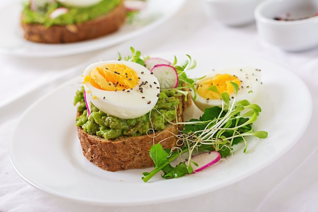 건강에 좋은 음식. 아침밥. 흰색 나무 테이블에 곡물 빵과 아보카도 계란 샌드위치.