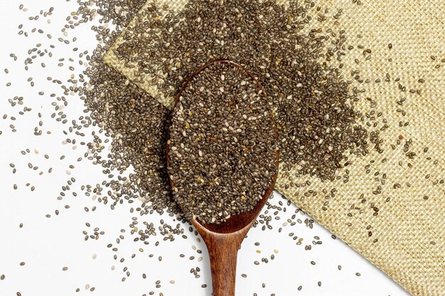 Photo healthy food chia seeds or superfood in wooden spoon falling on linen cloth over white background