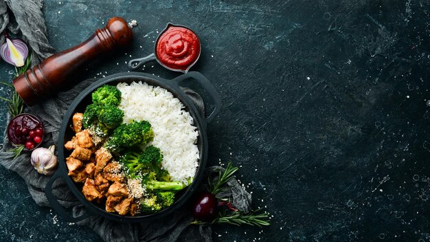 Cibo sano pollo con salsa teriyaki riso bollito e broccoli in una padella nera stile rustico vista dall'alto