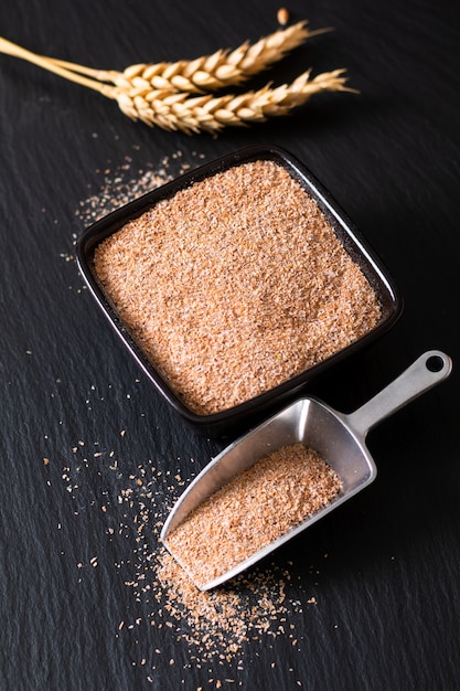 健康食品のコンセプト黒いスレート石に小麦の耳と黒いセラミックカップで有機小麦ふすま