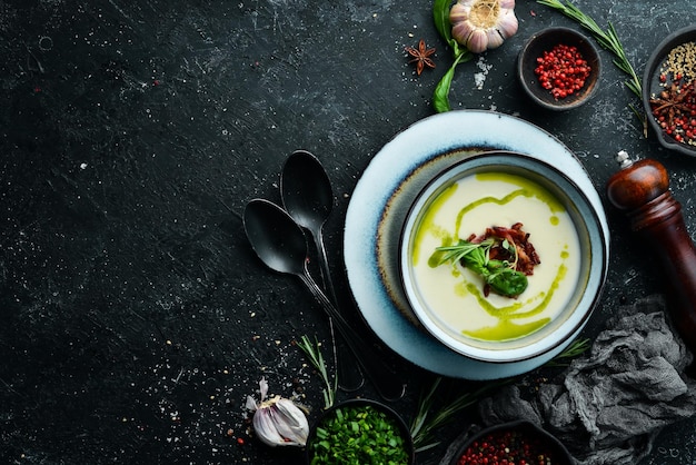 Photo healthy food creamy soup with bacon and basil in a plate on a black stone background top view rustic style