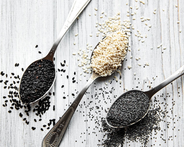 Foto cibo sano e concetto di bevande. semi di sesamo in bianco e nero e semi di papavero in cucchiai su un tavolo di legno