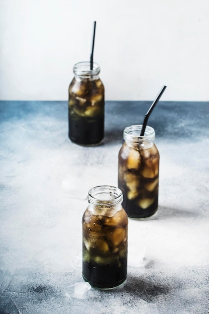 Healthy food and drink concept cold black detox mineral water with crushed ice in glass bottles with activated charcoal gray stone table background trendy beverage copy space selective focus