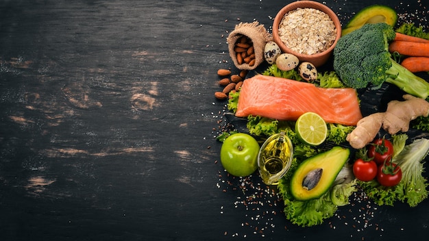 Healthy food Fish salmon avocado broccoli fresh vegetables nuts and fruits On a black background Top view Copy space